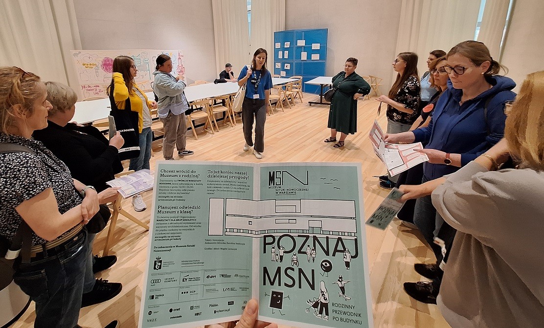 Grupa ludzi stojąca w kręgu, na pierwszym planie broszura z napisem "Poznaj MSN"