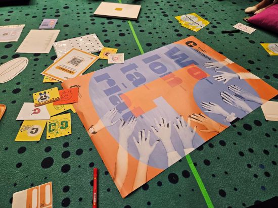 Plakat w kolorze pomarańczowo-fioletowym "Wolontariat - Teatr Guliwer", w tle zielona wykładzina w kropki