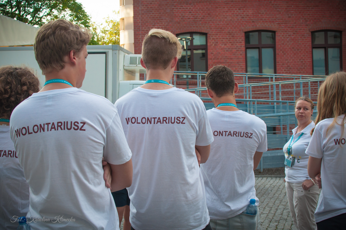 Wolontariusze z koszulkami z napisem "Wolontariusz" podczas odprawy wolontariuszy