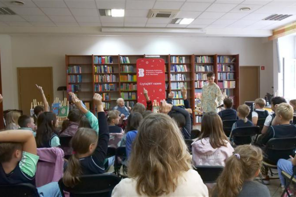 Spotkanie z autorką, panią Joanną Papuzińską. Na sali zgromadzona jest młodzież, niektóre z osób mają uniesione ręce.