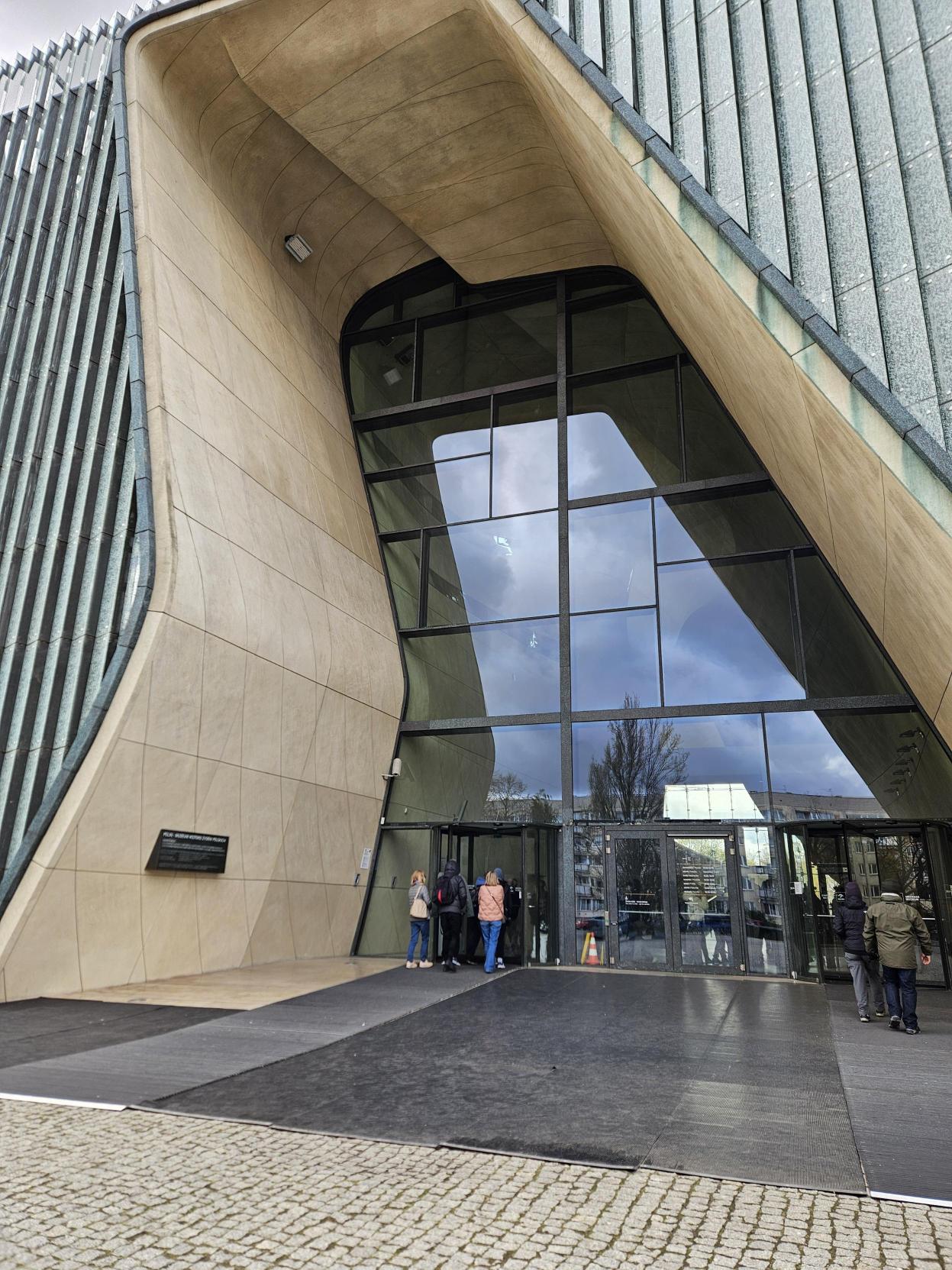 Ludzie stojący przed wejściem do budynku przypominającego rozstępującą się wodę.