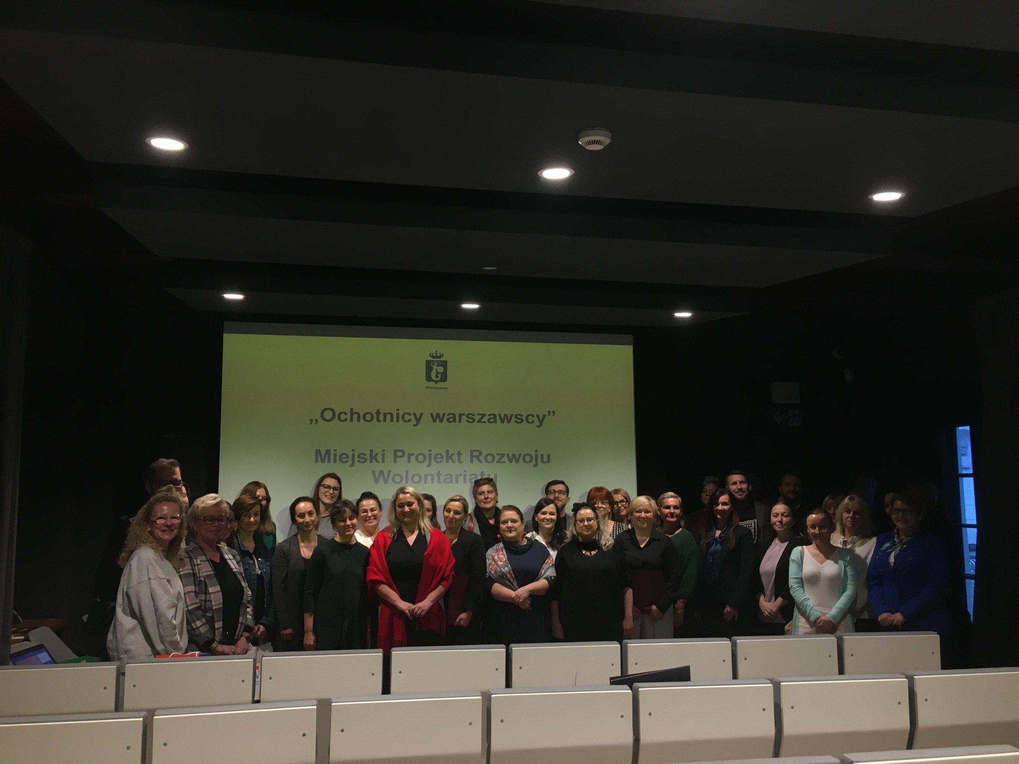 Grupa ludzi stojąca na tle slajdu "Ochotnicy warszawscy" Miejski Projekt Rozwoju Wolontariatu